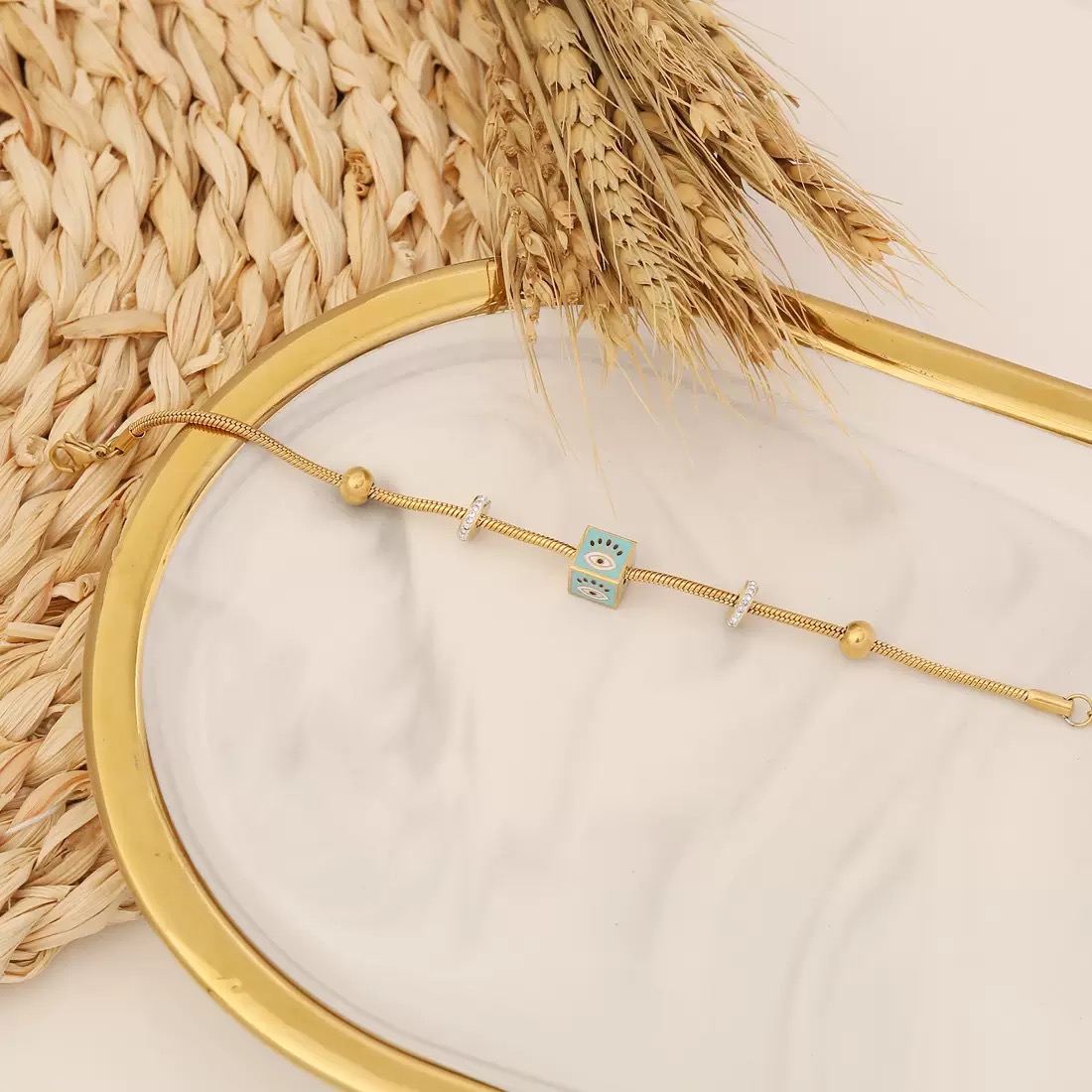 Liora 18K gold plated stainless steel snake chain bracelet featuring textured gold beads and a white and blue enamel evil eye cube charm with an adjustable extension chain.